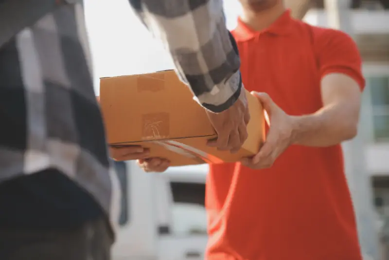 Ein Paket wird vor dem Haus von Hand zu Hand übergeben